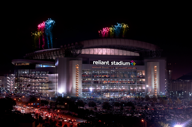 Nighttime view of Reliant Stadium with yellow, pink, and blue fireworks coming out of the top