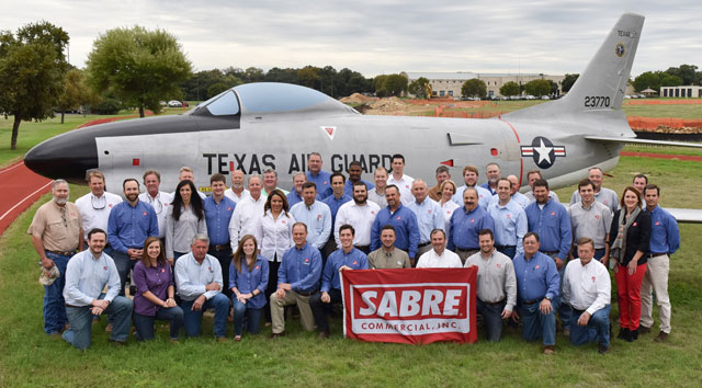 A group of people holding a SABRE Commercial, Inc banner in front of a Texas Air Guard jet