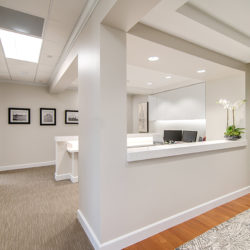 An office with a glass door entrance, gray carpets, and an open desk area next to the entrance.