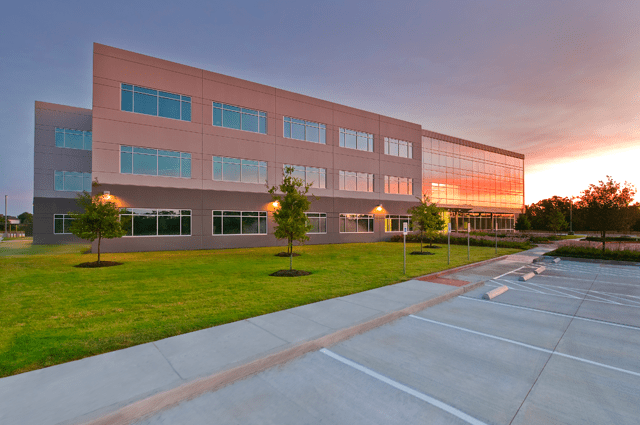 A gray 3 story building with large rectangular windows and there is a sunset reflecting on the building