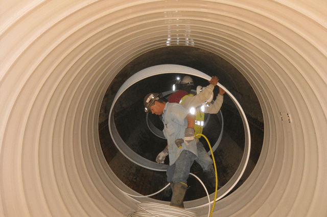 People standing in a sewer tunnel wearing hard hats with lights