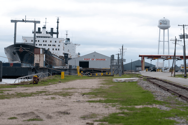 The Port of Orange building next to a yard and a large ship pulling up to the shore